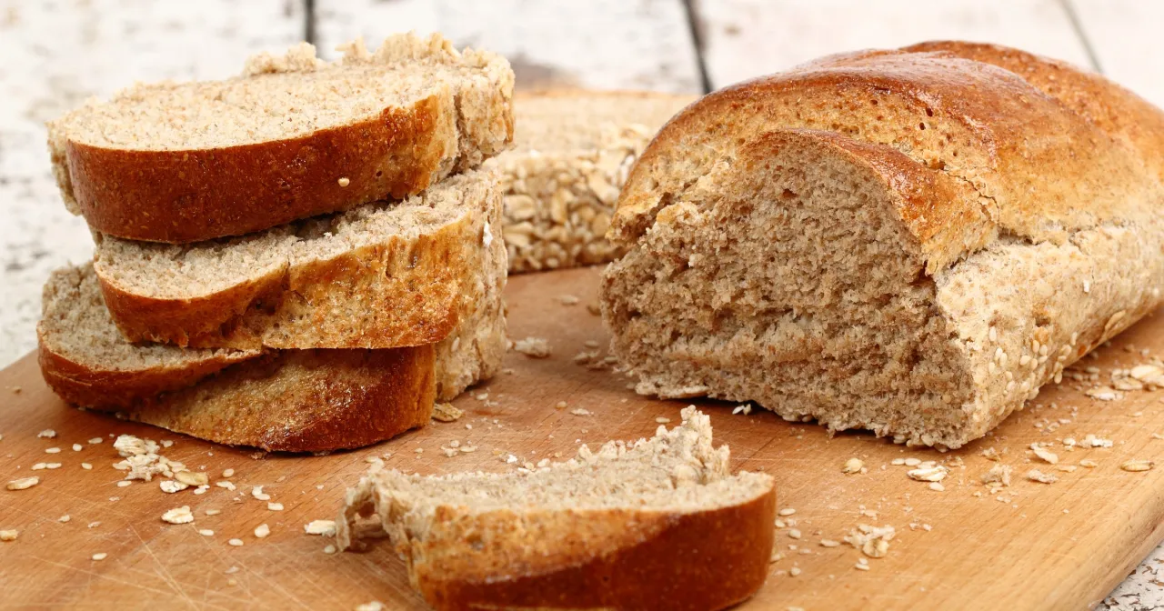 Krojony chleb graham na desce, posypany płatkami owsianymi i sezamem. Czy chleb graham jest dietetyczny? Tak, to świetny wyb&oacute;r!