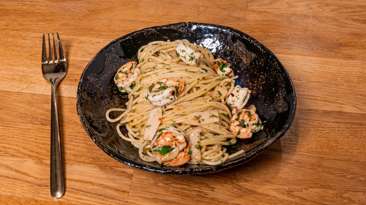 Pyszne dania z krewetkami: spaghetti z czosnkiem, pietruszką i soczystymi krewetkami na czarnym talerzu. Obok leży widelec.