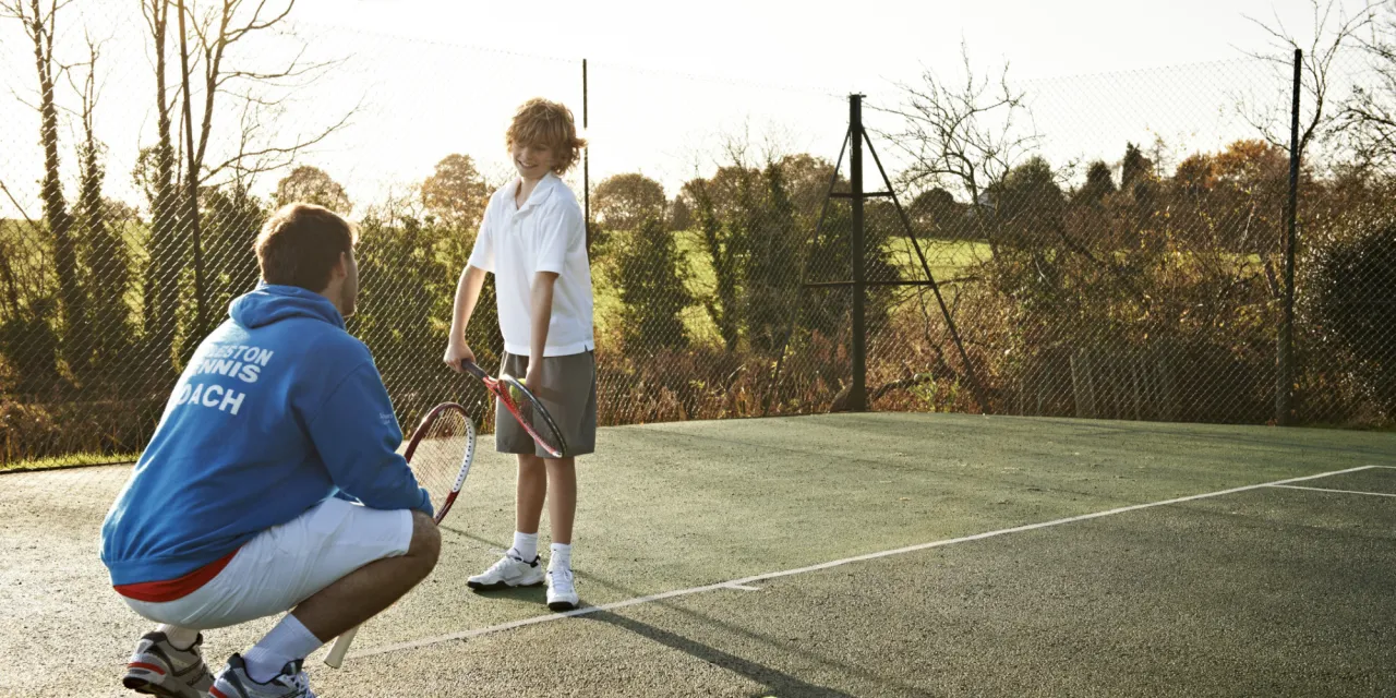 rodzic rozmawiający z trenerem na tle obiektu sportowego