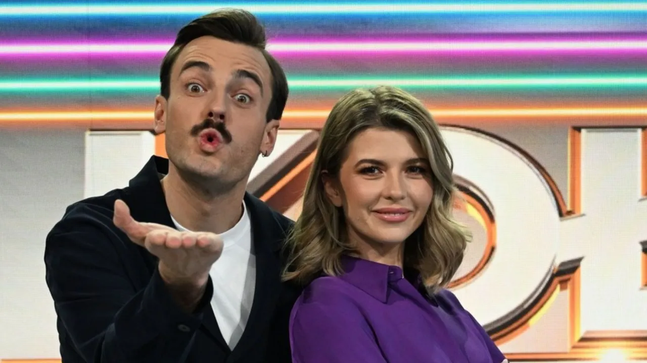 Uśmiechnięta para na tle kolorowych świateł, gdzie jest nagrywane Koło Fortuny.