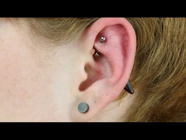 osoba odkręcająca kolczyk w uchu w rękawiczce