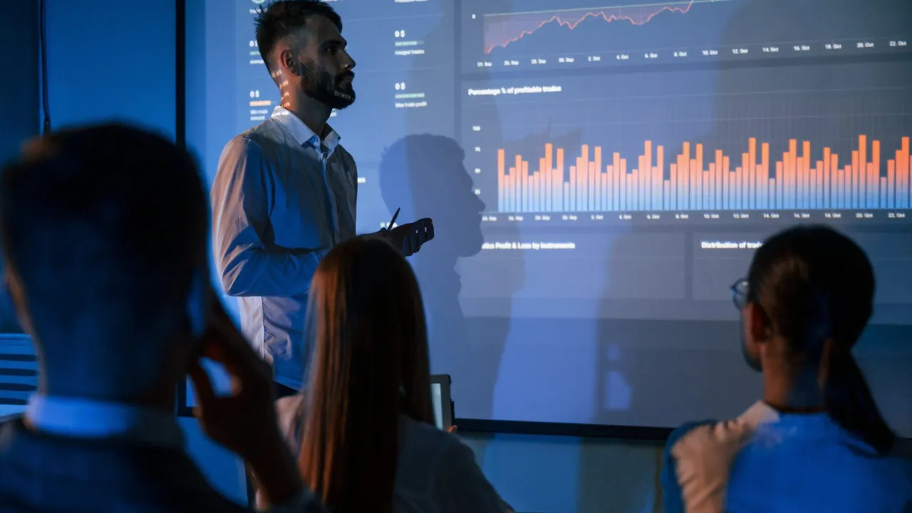 Prezentacja danych z Yandex Metrica: mężczyzna omawia wykresy zysk&oacute;w i strat, słuchacze analizują wyniki.