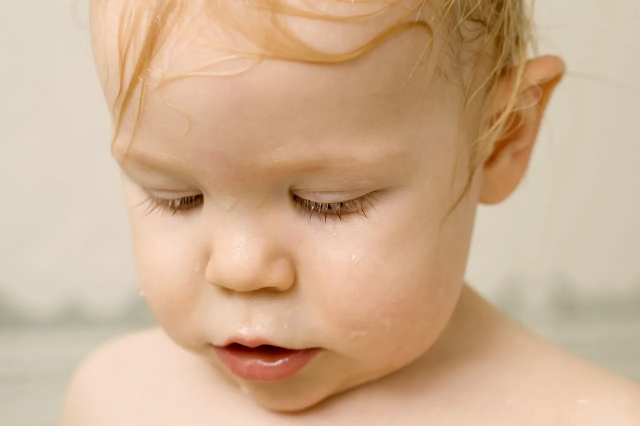 Urocze niemowlę się poci, z mokrymi włoskami i kropelkami wody na skórze.