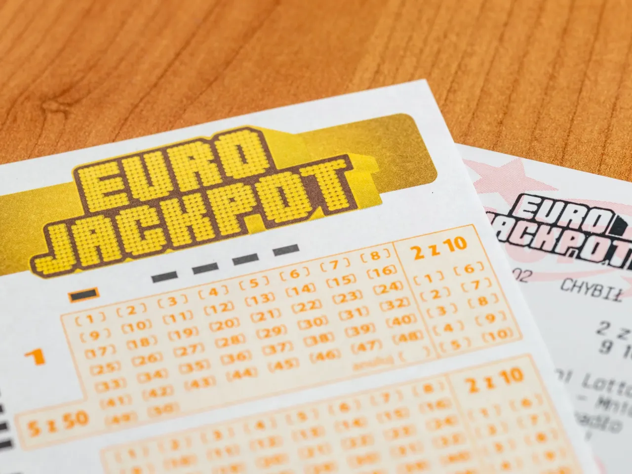 Kupony Eurojackpot leżą na drewnianym blacie. Zastanawiasz się, eurojackpot ile za 2 z 12?