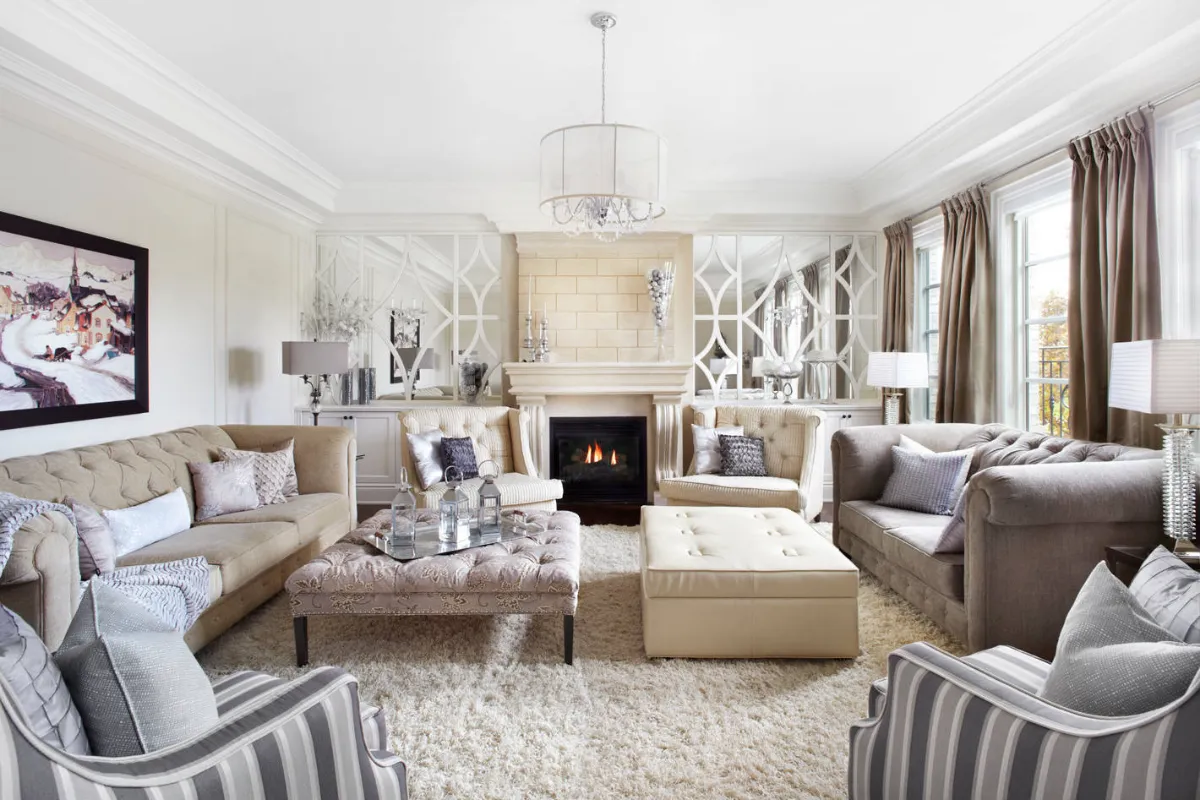 Elegancki salon z kominkiem, sofami i fotelami w odcieniach beżu i szarości. Widać, jak wygląda kolor ecru na pufie i poduszkach.