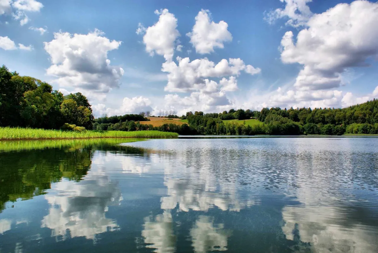 Spokojne jezioro na Kaszubach, z zielonymi wzgórzami i lasami w tle. Idealne miejsce, by odpocząć i zobaczyć, co warto zobaczyć na Kaszubach.
