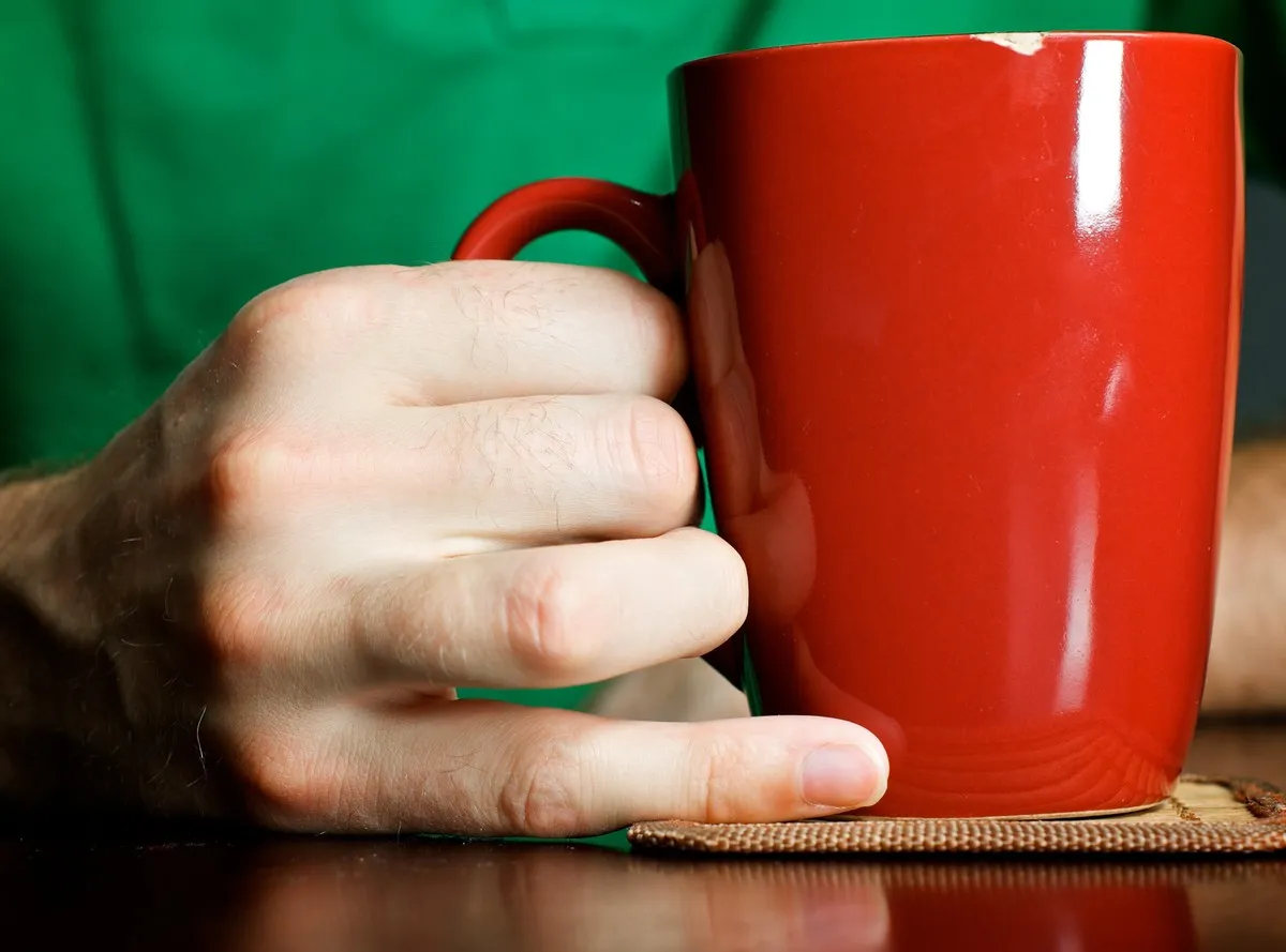 Dłoń trzymająca czerwoną filiżankę. Czy herbata wysusza organizm? To pytanie nurtuje wielu miłośników tego napoju.