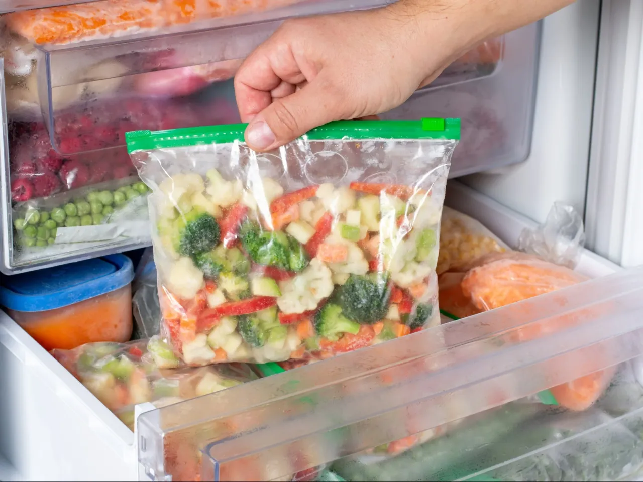 Mrożonka warzywna w torebce: brokuły, kalafior, marchewka, papryka. W zamrażarce widać też groszek i inne warzywa, kt&oacute;re można mrozić.