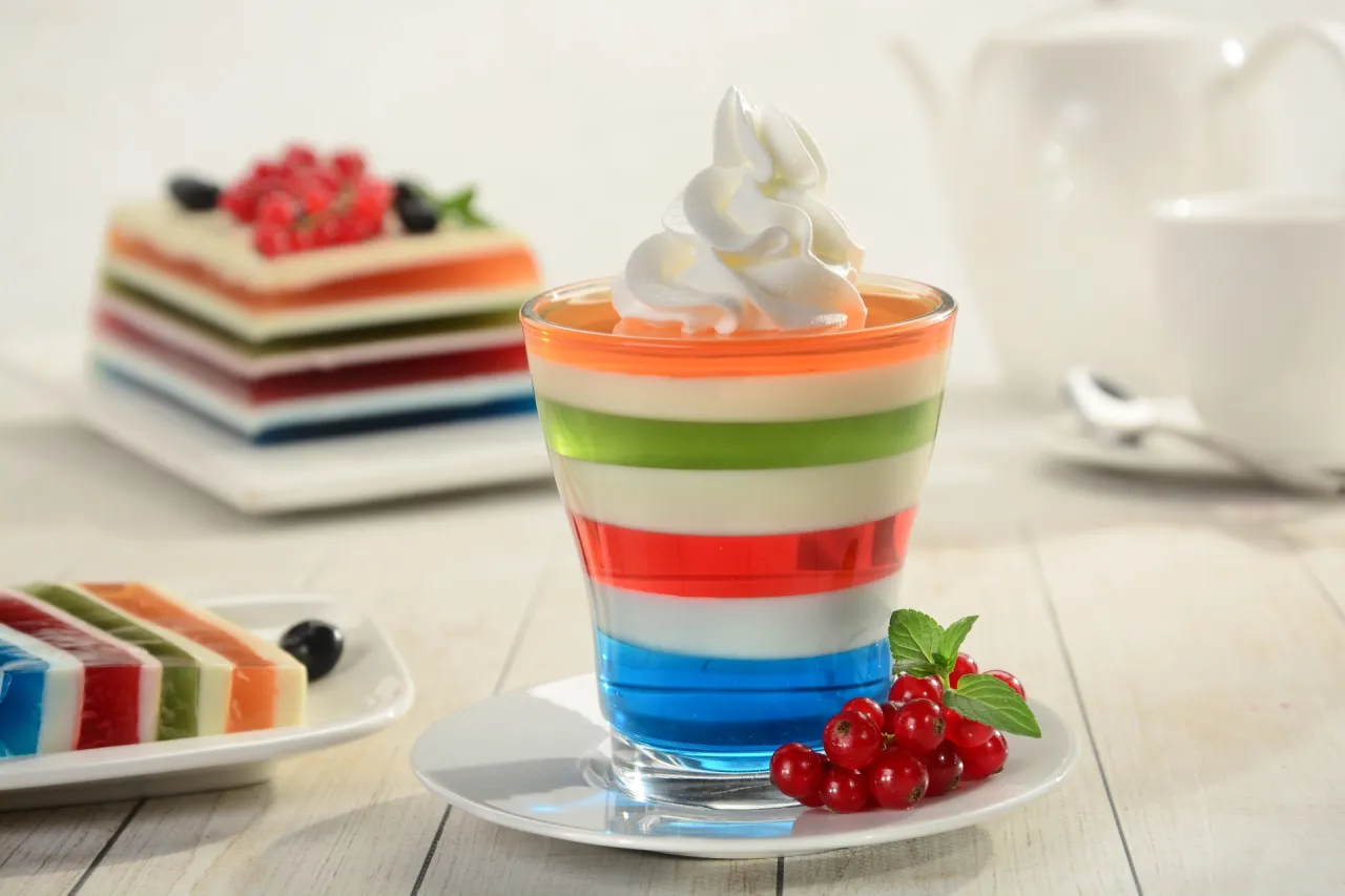 Kolorowa galaretka w szklance, udekorowana bitą śmietaną i porzeczkami. Obok kawałek ciasta z galaretki. Czy galaretkę można ponownie rozpuścić?