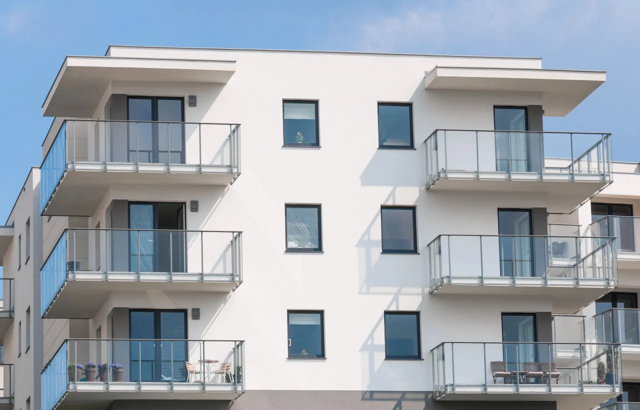 Nowoczesne osiedle mieszkanie plus z balkonami i szklanymi balustradami, w tle błękitne niebo.