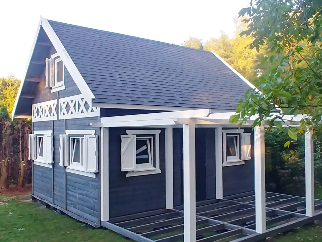 Nowy domek na działkę ROD z ciemnoszarymi ścianami, białymi okiennicami i werandą.