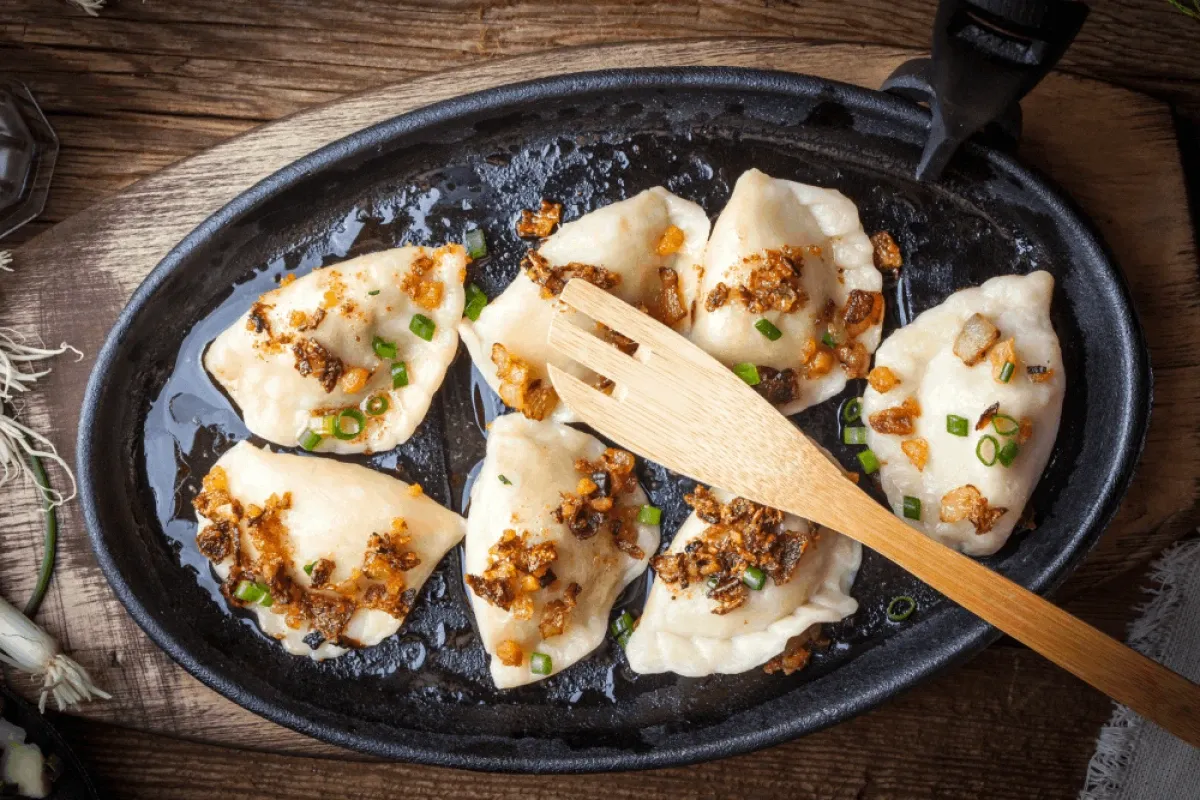 Pyszne pierogi ruskie na patelni, posypane skwarkami i szczypiorkiem. Idealne, by pokazać, jak zrobić pierogi ruskie.