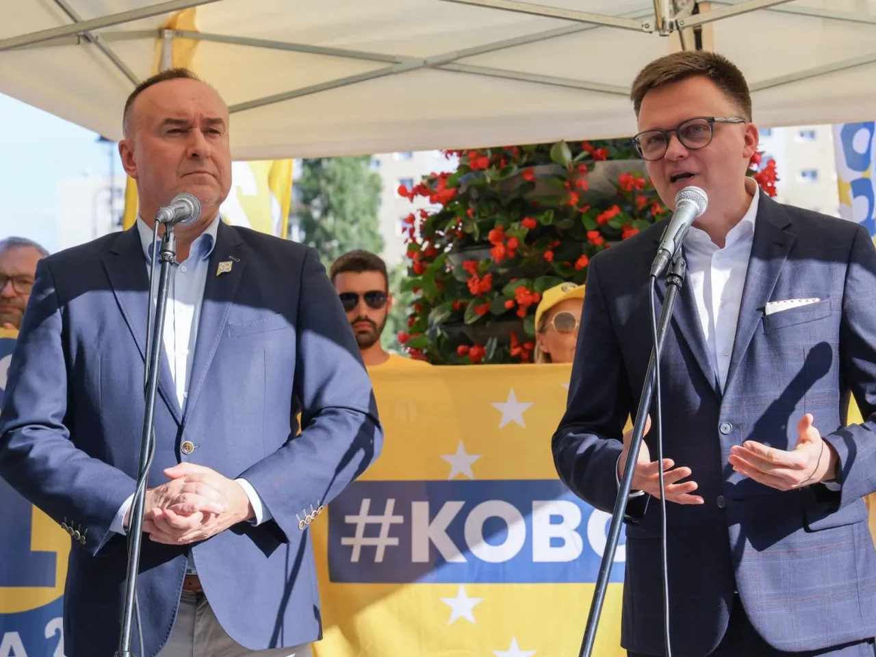 Dwóch mężczyzn przemawia przy mikrofonach na tle banera z napisem #KOBOSZ. Czy to ukryte przyczyny odejścia Michała Kobosko z koalicji i oskarżenia o dyktaturę?