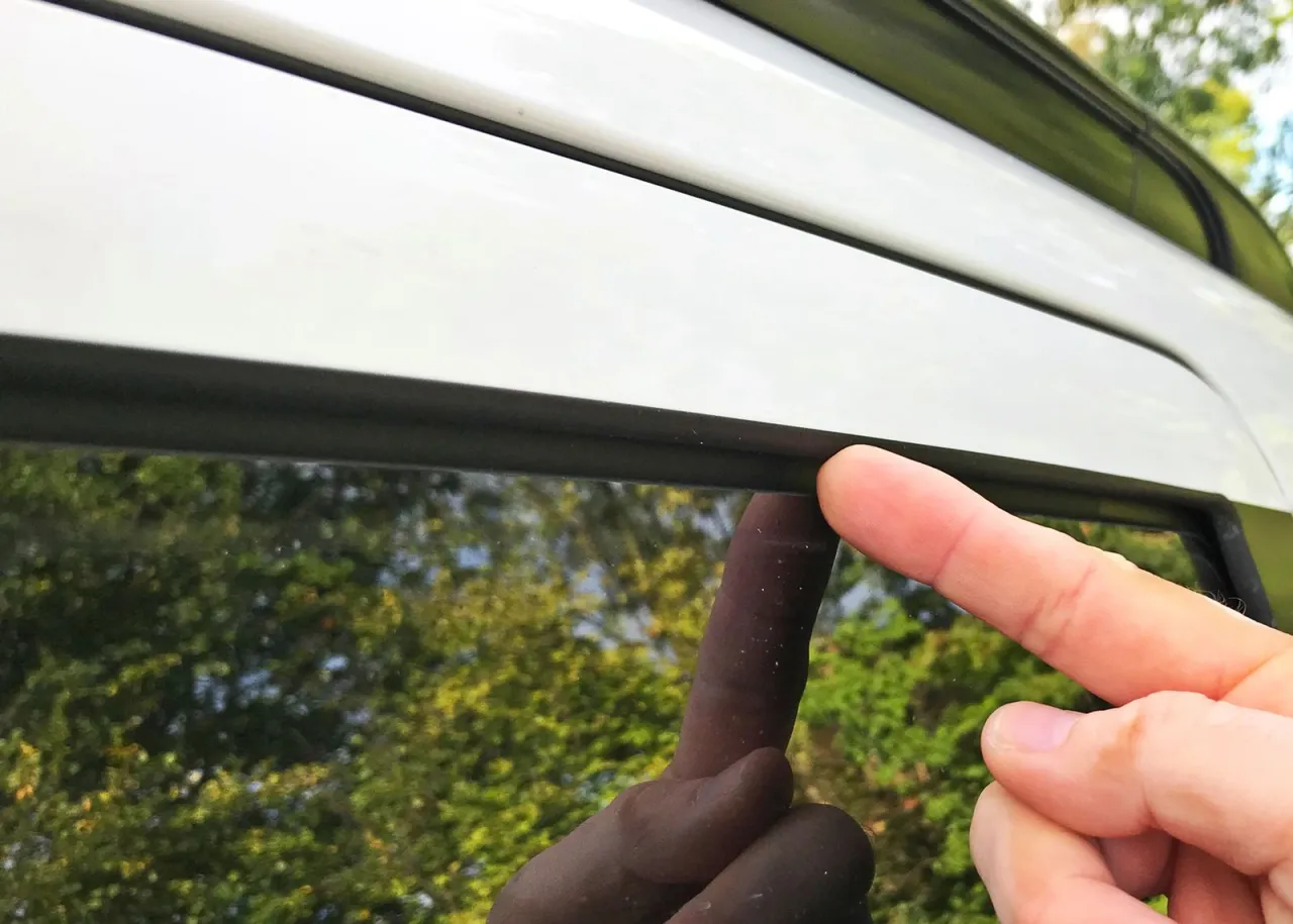 Palec wskazuje na uszczelkę okna, gdzie może gromadzić się woda w samochodzie z tyłu.