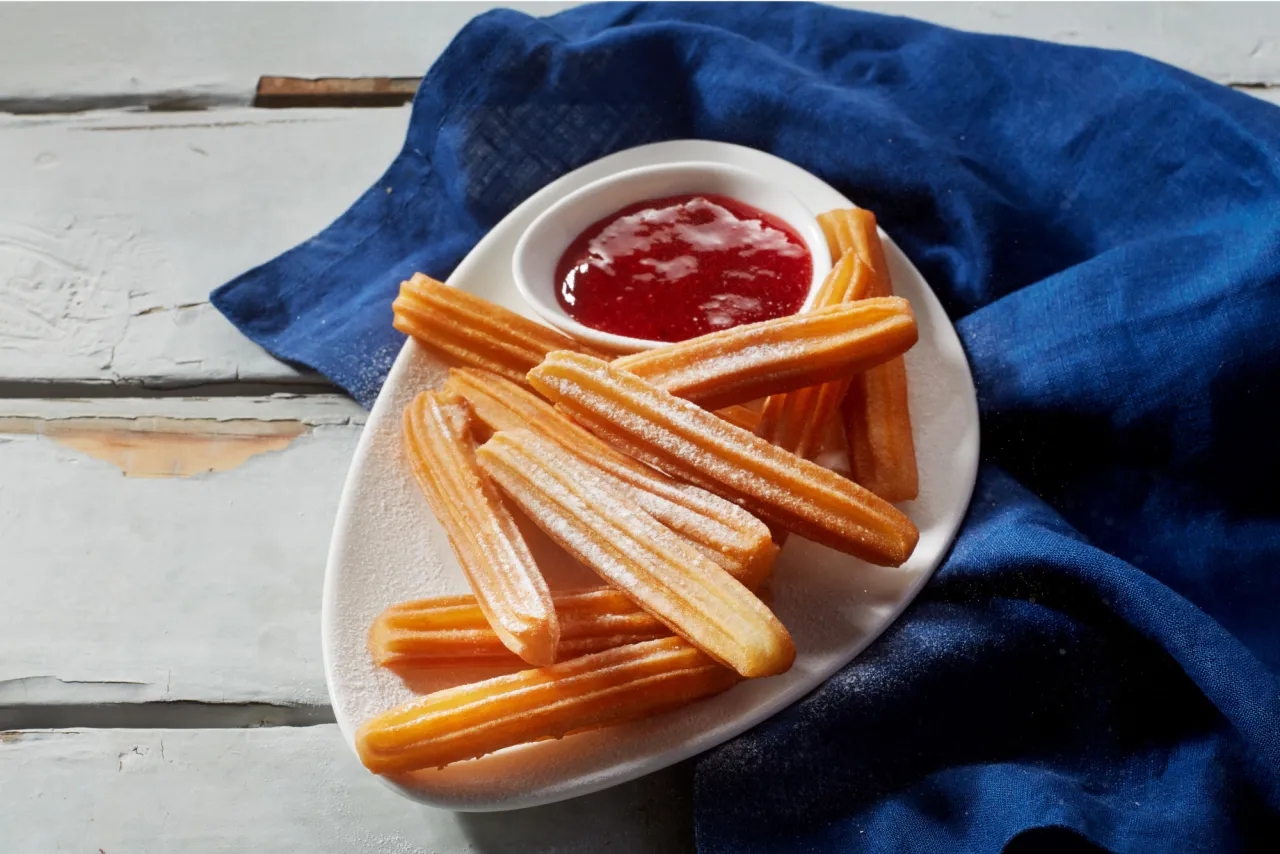 Churros przepis: złociste, posypane cukrem pudrem paluszki z ciasta smażonego na głębokim tłuszczu, podane z konfiturą.