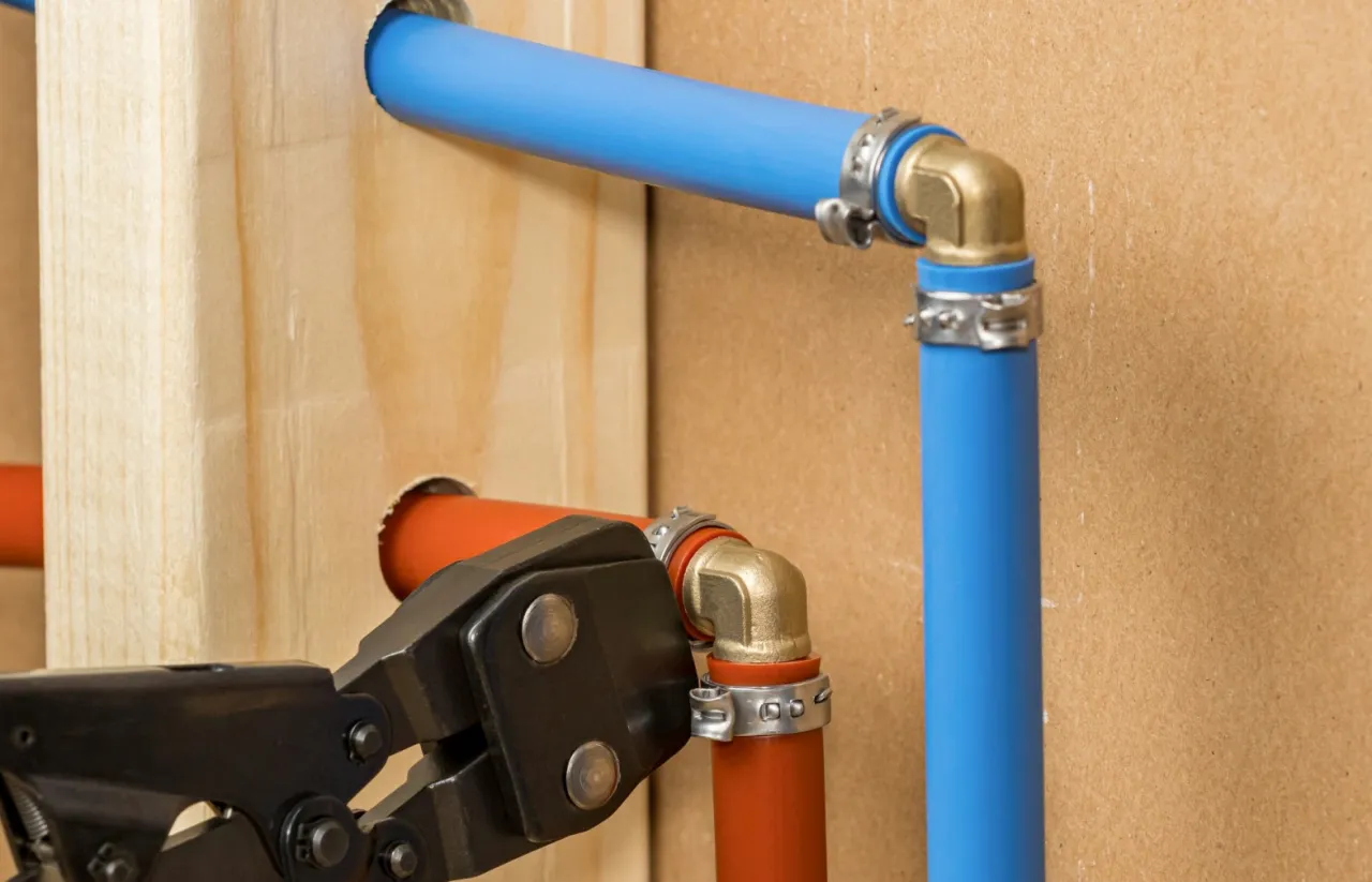 Instalacja hydrauliczna z rurą PEX do CO. Narzędzie zaciska złączkę na pomarańczowej rurze, obok niebieska rura PEX.