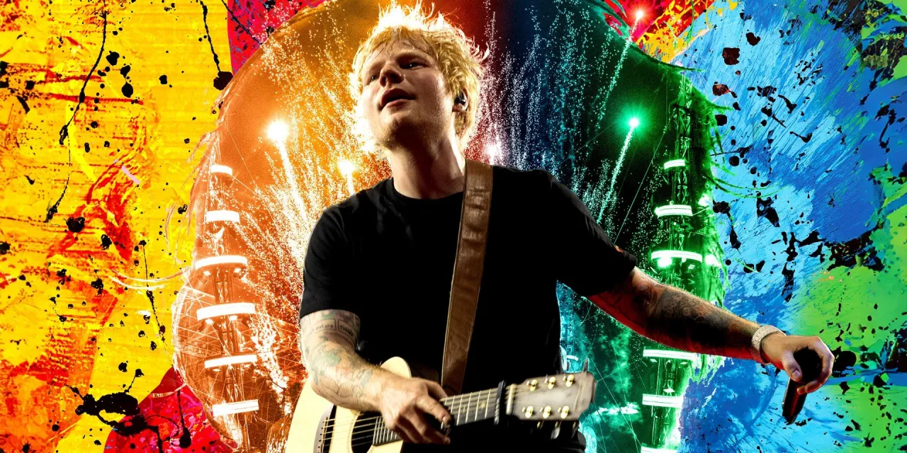 Ed Sheeran gra na gitarze na tle kolorowych eksplozji. Zastanawiasz się, ile zarabia Ed Sheeran?
