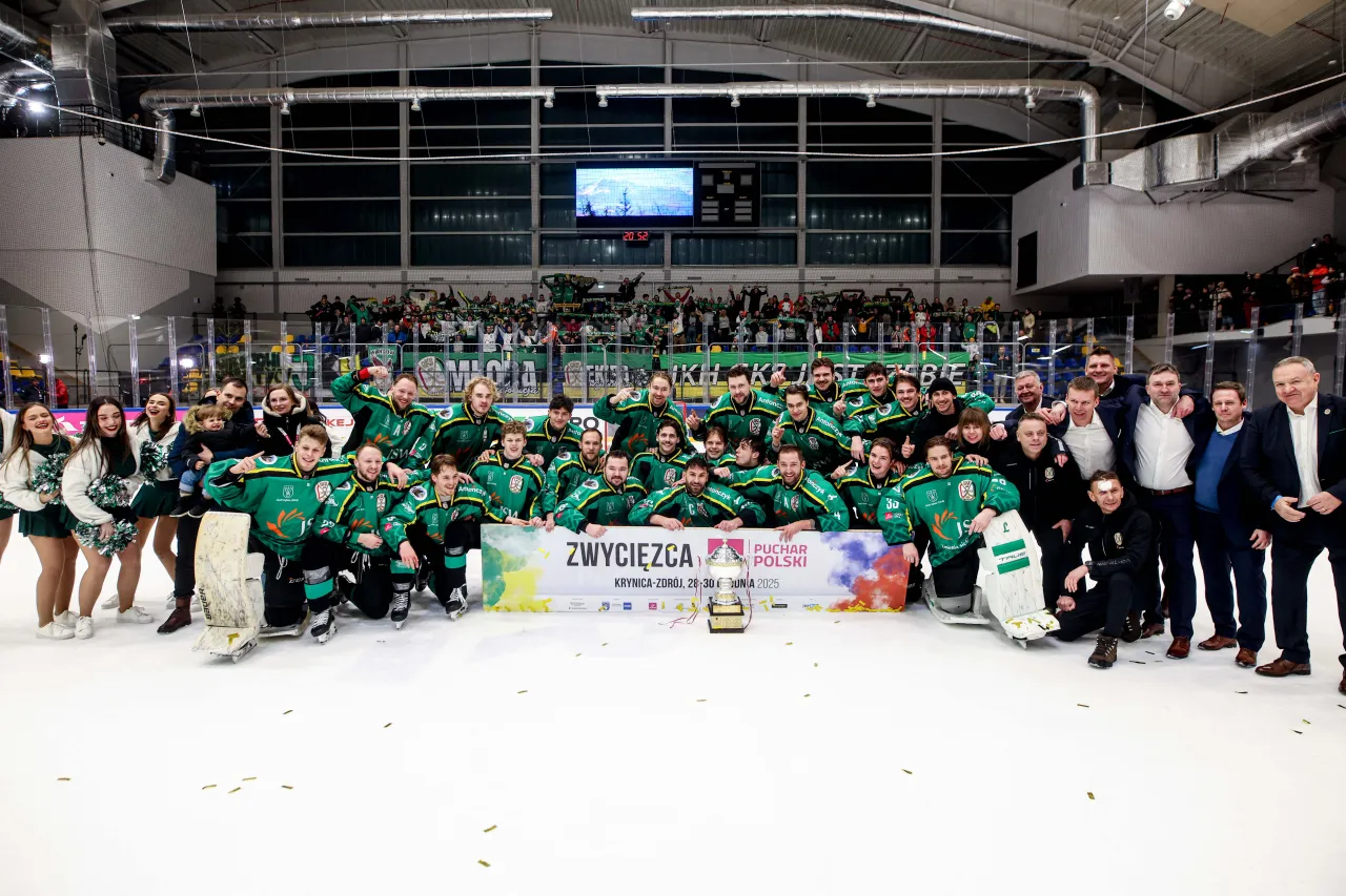 Drużyna w zielonych strojach świętuje zwycięstwo w Pucharze Polski w piłce nożnej, pozując z pucharem i kibicami.