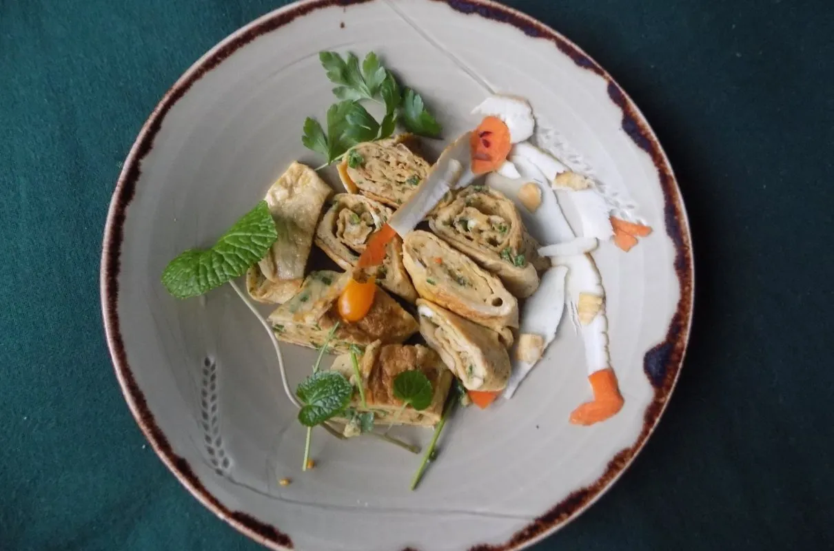 Roladki sushi w omlecie, ozdobione marchewką i ziołami, wyglądają jak mała postać w stroju kosmonauty.