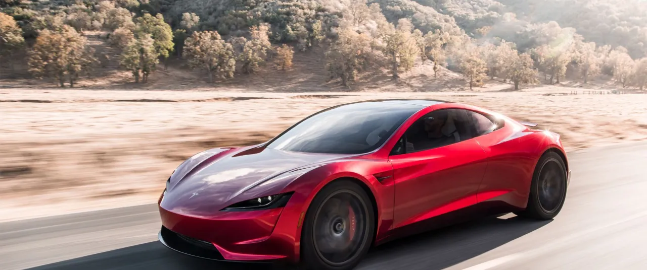 Czerwony Tesla Roadster pędzi po pustynnej drodze. Zastanawiasz się, ile kosztuje Tesla Roadster?