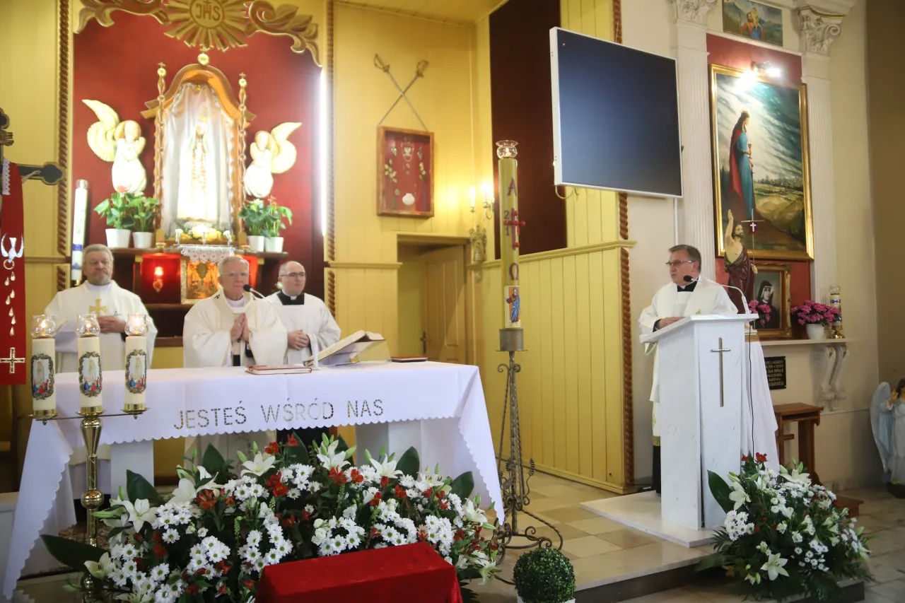 Uroczystość bierzmowania w kościele. Księża w strojach liturgicznych, ołtarz ozdobiony kwiatami.
