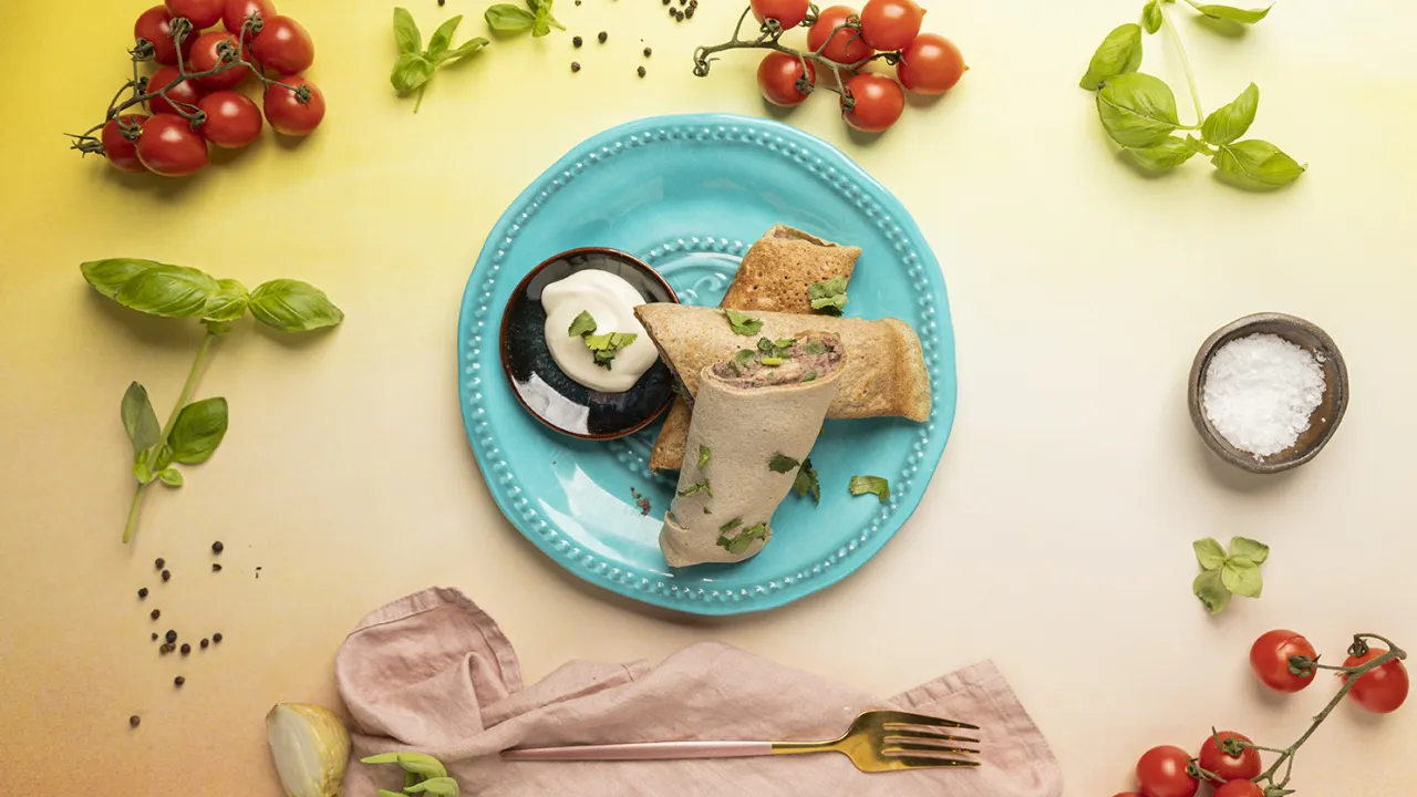 Gotowy przepis na zdrowe naleśniki: zawinięte naleśniki z farszem, podane z sosem śmietanowym, pomidorkami i bazylią.