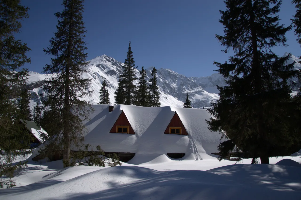 Zimowy krajobraz Tatr z zasypanym śniegiem schroniskiem. Idealne miejsce na wędr&oacute;wkę, jeśli zastanawiasz się, jaki szlak zimą w Tatrach wybrać.