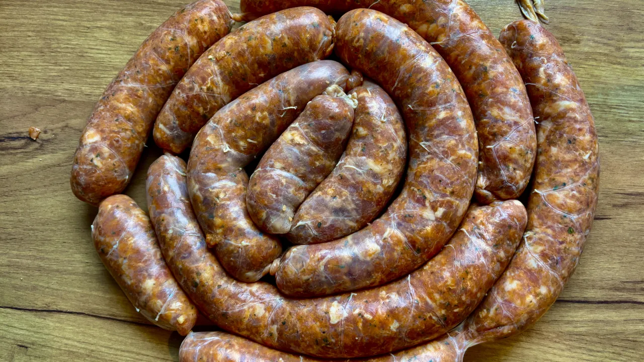 Surowe kiełbaski ułożone w okrąg na drewnianym blacie. Zastanawiasz się, ile czasu moczymy jelita do kiełbasy?