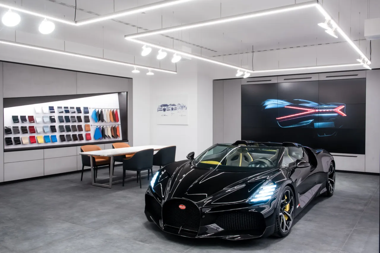 Czarny Bugatti w salonie, obok próbek kolorów i ekranu z tyłem auta. Zastanawiasz się, ile kosztuje Bugatti?