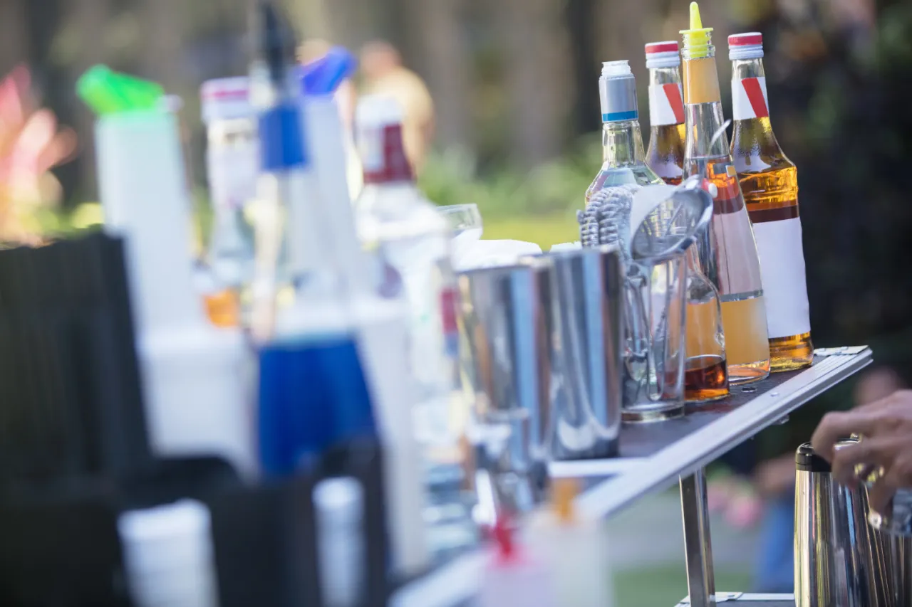 Kolorowe butelki z syropami i alkoholem, metalowe shakery i sitka tworzą nowoczesny drink bar zamiast barmana.