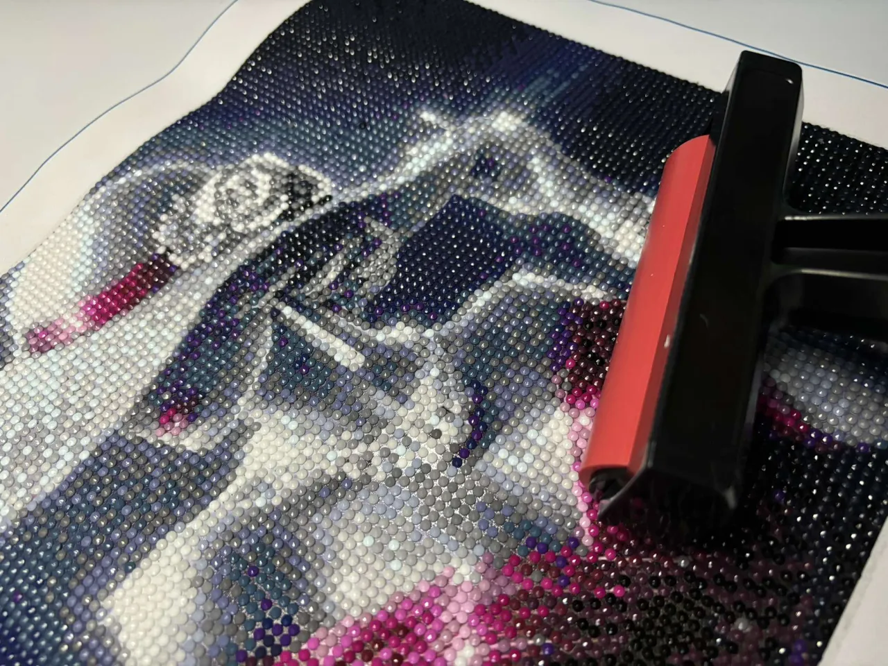 Haft diamentowy jak zrobić? Obraz z jednorożcem w trakcie tworzenia, z narzędziem do dociskania kamyczk&oacute;w.