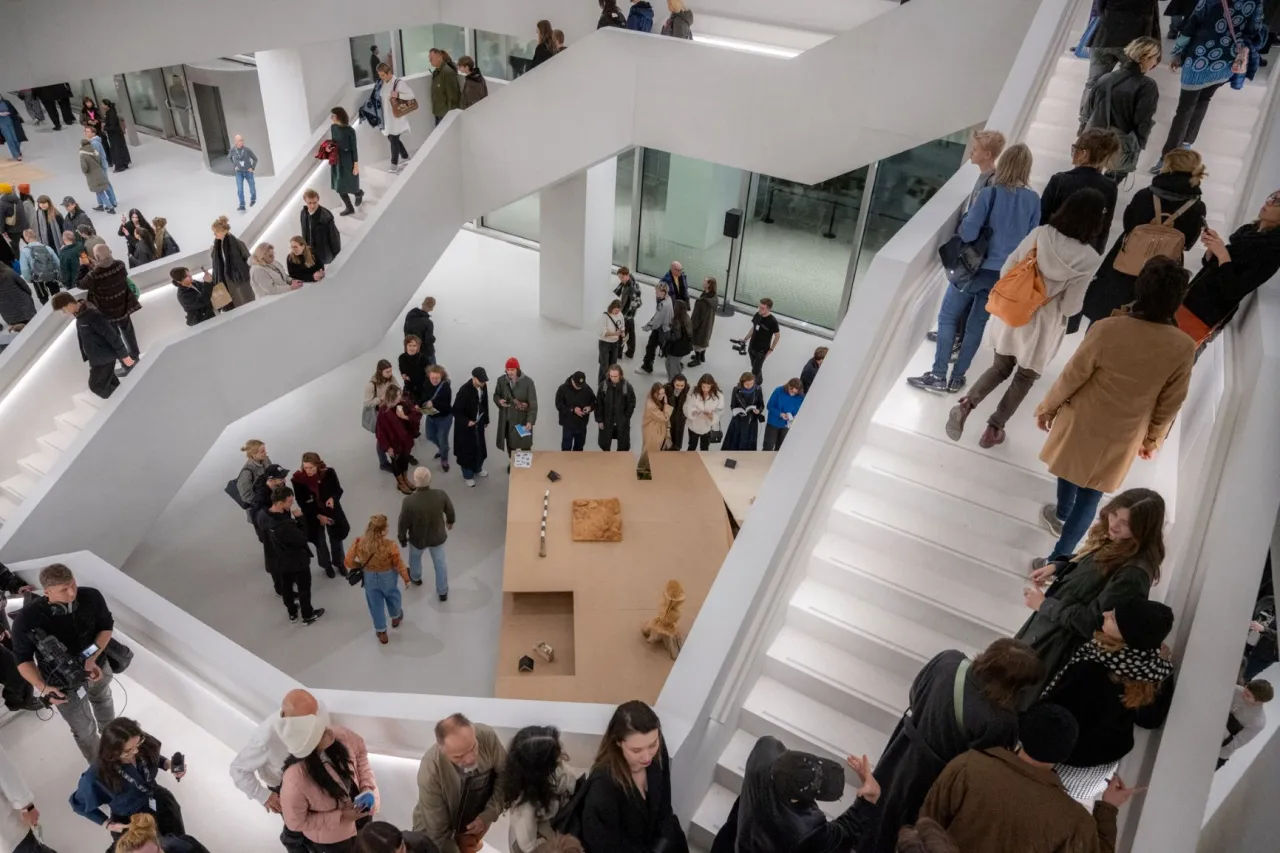 Zwiedzający w nowoczesnym wnętrzu muzeum sztuki wsp&oacute;łczesnej Warszawa, poruszający się po białych schodach i platformach, podziwiający ekspozycję.