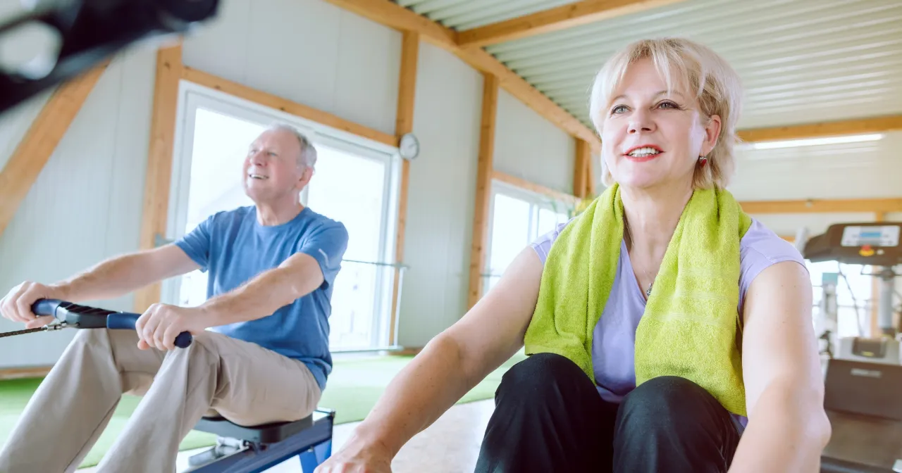 Para schudnąć, jak ćwiczyć na wioślarzu? Uśmiechnięci seniorzy trenują razem, motywując się nawzajem do wysiłku.