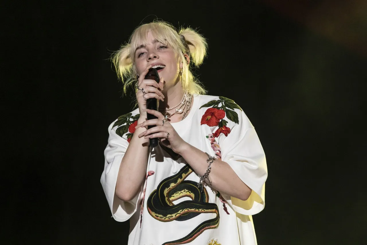 Billie Eilish śpiewa na koncercie w białej bluzce z wężem i kwiatami. Zastanawiasz się, ile kosztuje bilet na koncert Billie Eilish?