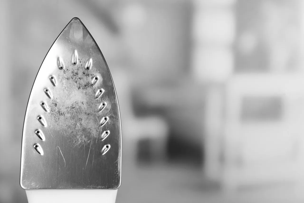 Metalowa stopa żelazka z widocznymi otworami na parę, lekko zabrudzona. Dowiedz się, jak odkamienić stację parową, by prasowanie było efektywne.