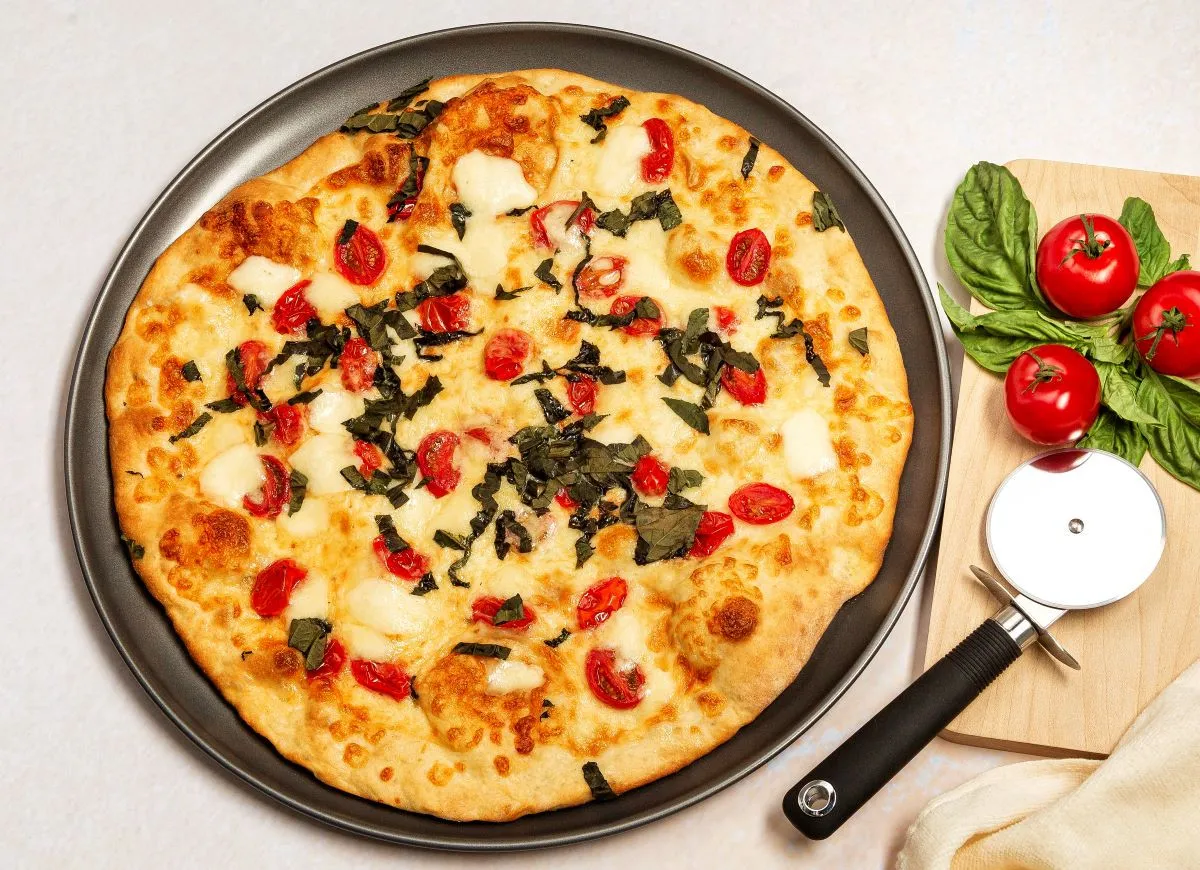 Pyszna pizza z serka wiejskiego, pomidorkami koktajlowymi i bazylią, gotowa do pokrojenia.