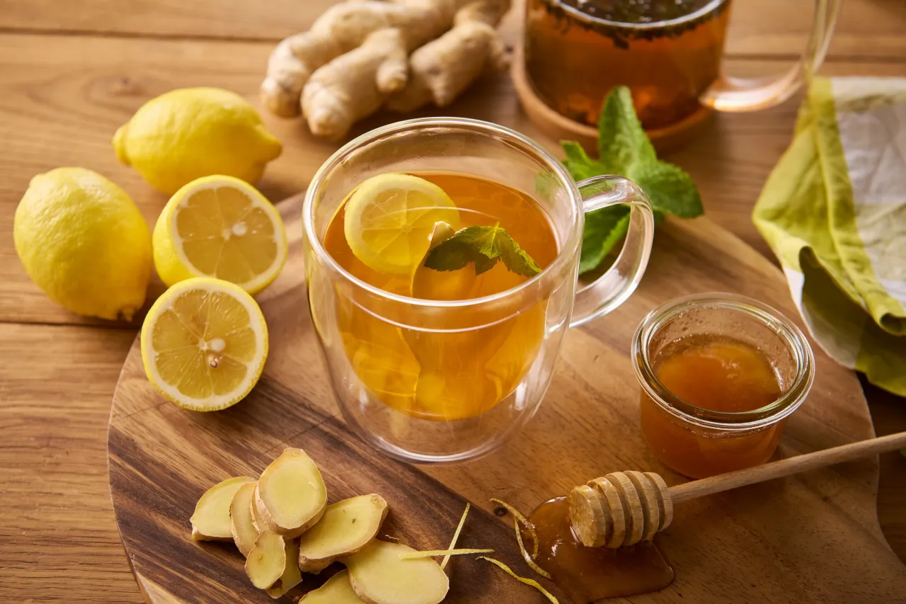 Jak dodać imbir do herbaty? Na stole leżą cytryny, plasterki imbiru, miód i gotowy napar.