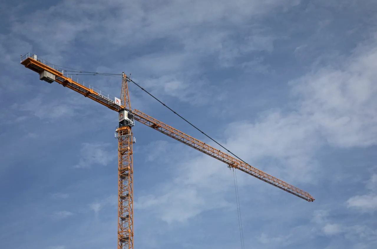 Pomarańczowy dźwig budowlany na tle błękitnego nieba z chmurami. To maszyna, kt&oacute;ra pomaga wznosić budynki.