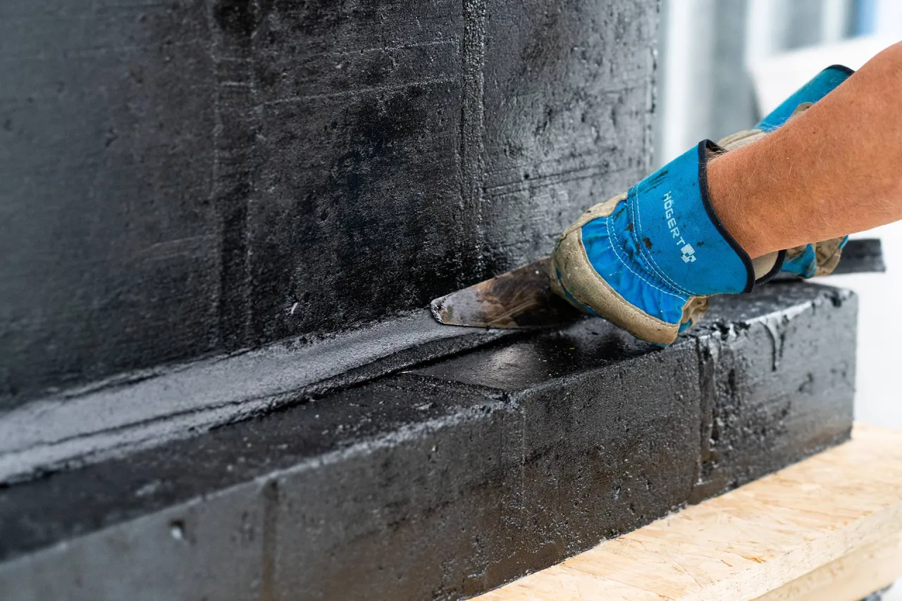 Rękawica z narzędziem uszczelnia czarne fundamenty. To ważny etap prac, by wiedzieć, czym obsypać fundamenty po hydroizolacji.