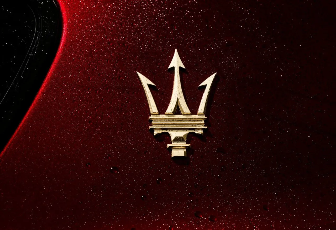 Złoty tr&oacute;jząb, jak wygląda znaczek Maserati, lśni na tle ciemnoczerwonego, mokrego lakieru.