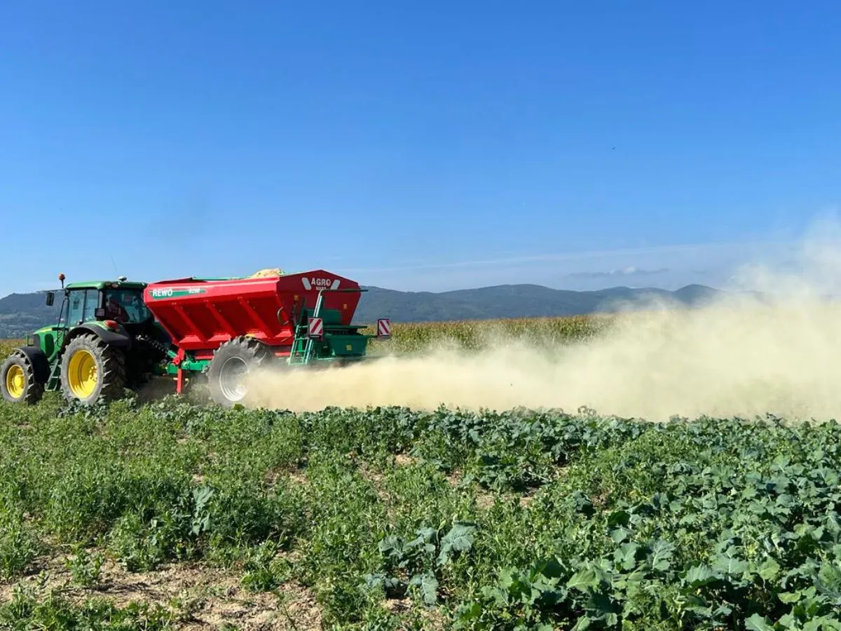 Traktor z rozsiewaczem wapna na polu. Dofinansowanie na takie zabiegi jest kluczowe dla rolnictwa.