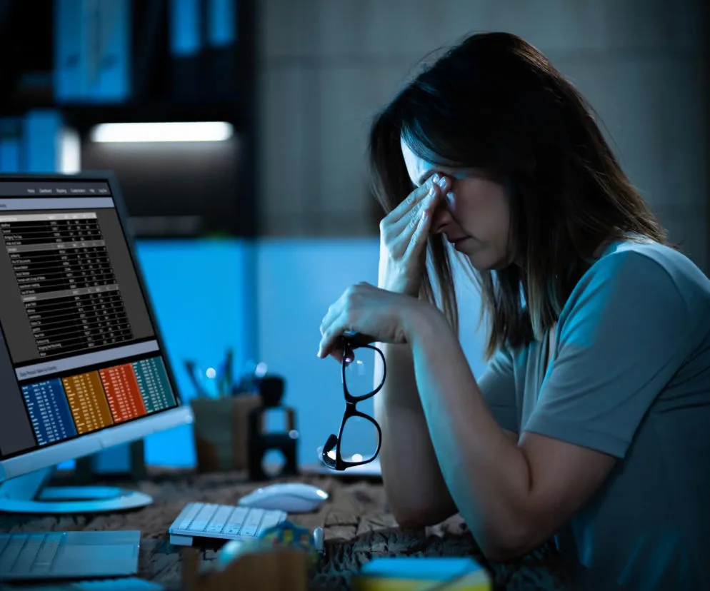 osoba odczuwająca zmęczenie oczu przed komputerem w ciemnym pokoju