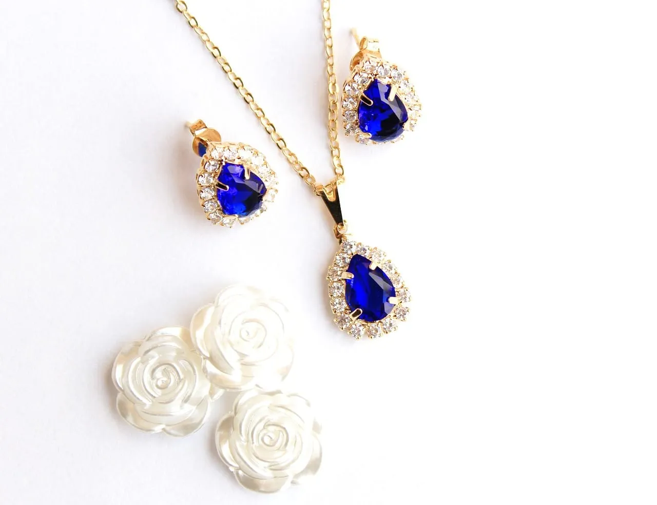 Złota biżuteria z niebieskimi kamieniami, przypominającymi metale p&oacute;łszlachetne, i białe r&oacute;życzki.