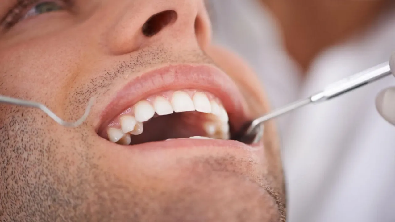 Mężczyzna z b&oacute;lem zęba w Koninie u dentysty. Badanie jamy ustnej narzędziami stomatologicznymi.