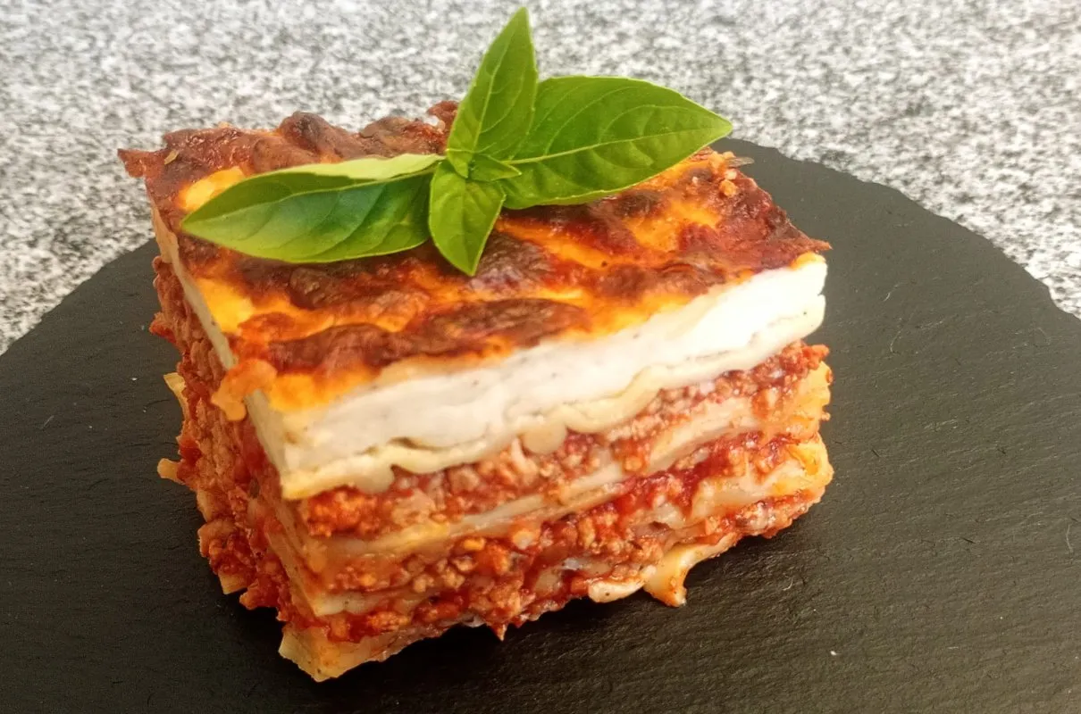 Pyszna lasagna z mięsem mielonym, idealna odpowiedź na pytanie co ugotować z mięsa mielonego. Podana z listkami bazylii.