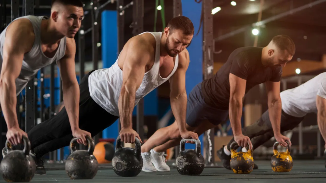 Mężczyźni wykonują pompki z kettlebellami, pokazując, jak połączyć crossfit z siłownią.