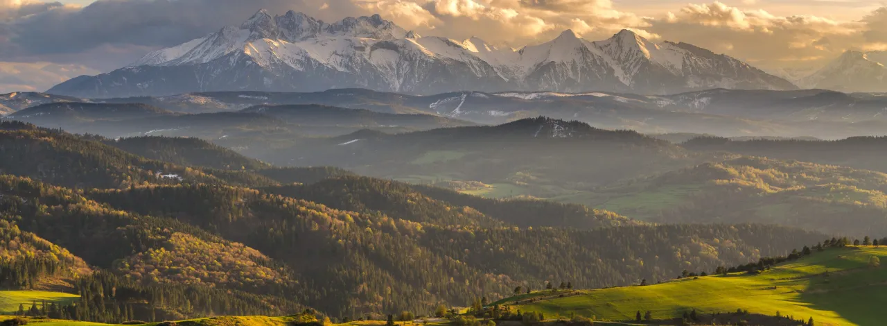 Piękne polskie g&oacute;ry, gdzie jechać latem? Tatry ośnieżone, a niżej zielone wzg&oacute;rza i lasy. Idealne na wakacje.