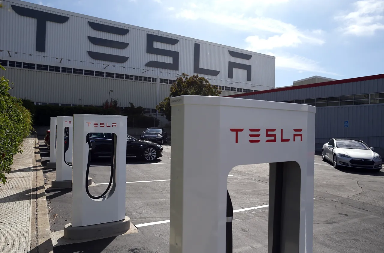 Ładowarki Tesli przed budynkiem z logo firmy. Tesla to marka z USA, znana z innowacyjnych samochod&oacute;w elektrycznych.