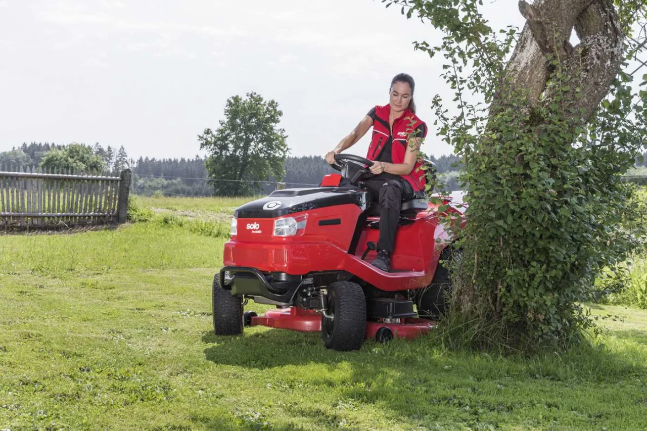 Kobieta na czerwonym traktorku ogrodowym, gotowa do koszenia. Dowiedz się, jak ustawić kosisko w traktorku, by uzyskać idealny trawnik.