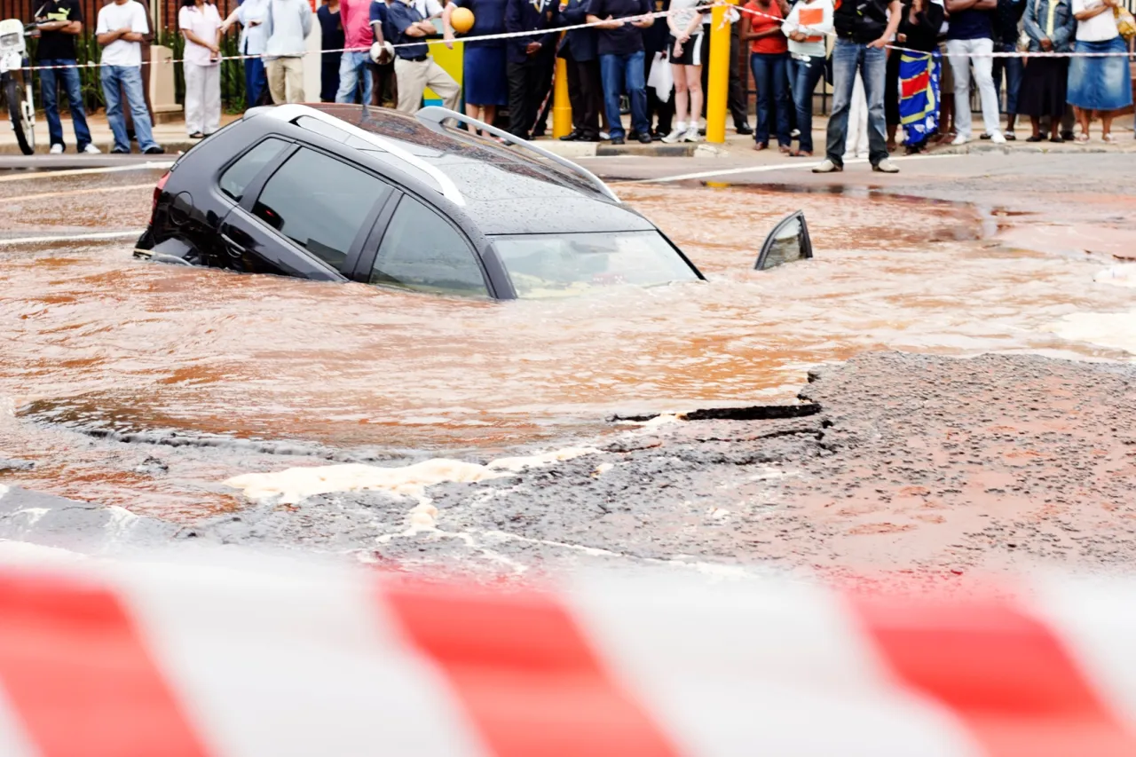 Czarny samoch&oacute;d tonie w brudnej wodzie po tym, jak kupiłem auto po powodzi. Ludzie obserwują z bezpiecznej odległości.